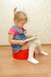 Little girl sitting on red potty with open book
