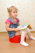 Little girl sitting on red potty with open book