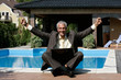 Happy businessman sitting next to the swimming pool