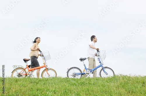 사진:自転車を押して丘の上を歩くカップル 自転車を押して丘の上を歩くカップル