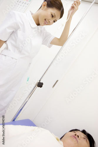 Photo: ベッドで横になる患者と点滴を準備する看護師 ベッドで横になる患者と点滴を準備する看護師