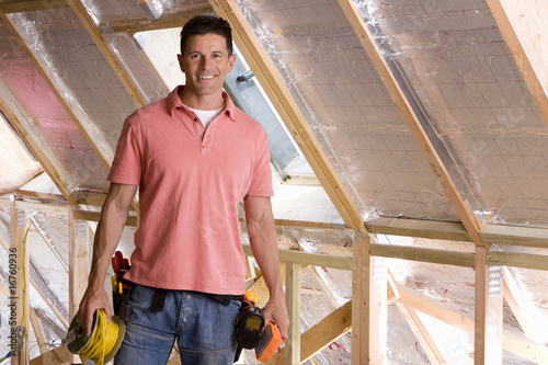 Photo: Smiling electrician standing in attic under construction Smiling electrician standing in attic under construction