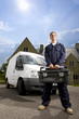 Handyman in coveralls holding toolbox near work van