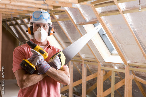 Photo: Construction worker wearing protective mask and holding tools in attic Construction worker wearing protective mask and holding tools in attic