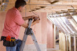 Electrician using meter on ladder in attic under construction