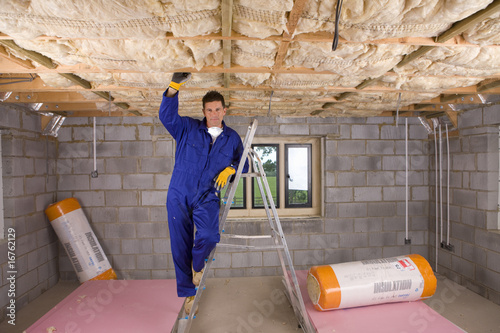 Photo: Man in coveralls and protective mask installing ceiling insulation Man in coveralls and protective mask installing ceiling insulation