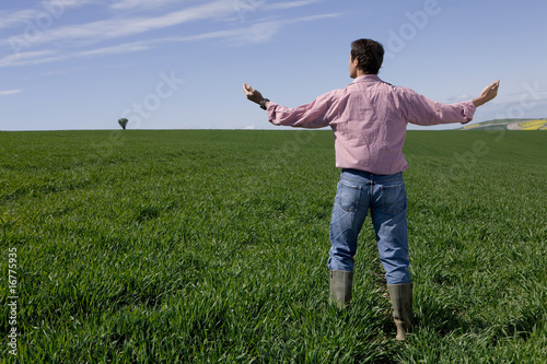 Photo: Farmer standing with arms outstretched in young wheat field Farmer standing with arms outstretched in young wheat field