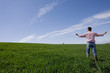 Farmer standing with arms outstretched in young wheat field