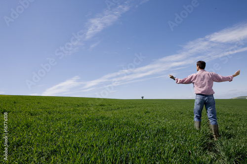 Photo: Farmer standing with arms outstretched in young wheat field Farmer standing with arms outstretched in young wheat field