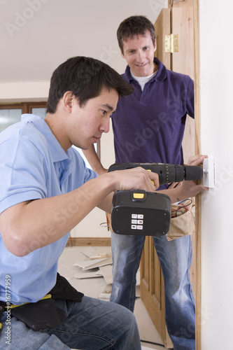 Photo: Electrician watching co-worker drill outlet in wall Electrician watching co-worker drill outlet in wall