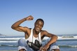 Man sitting on beach with with football boots round his neck cheering