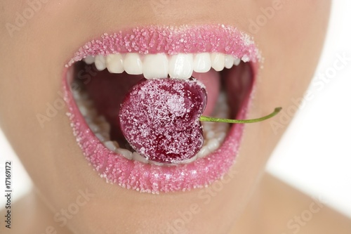 Photo: Cherry with sugar between woman teeth Cherry with sugar between woman teeth