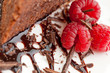 Three raspberries next to a slice of chocolate cake