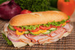 Tasty submarine sandwich with fresh produce in the background