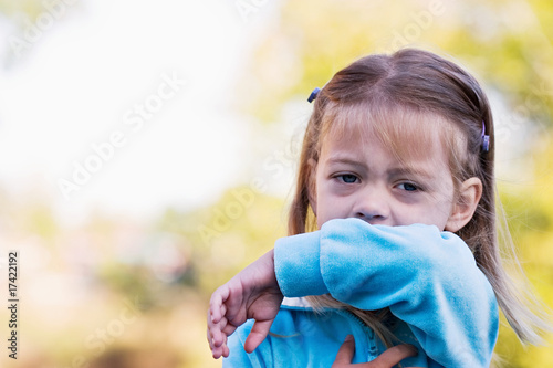 Photo: Little girl coughing or sneezing into her elbow. Little girl coughing or sneezing into her elbow.