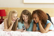 Group Of Three Teenage Girls Using Mobile Phone In Bedroom