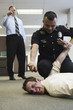 Police officer holding beat up businessman on floor in office