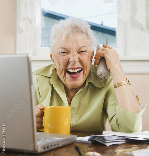 Foto: Senior woman paying bills and laughing Senior woman paying bills and laughing