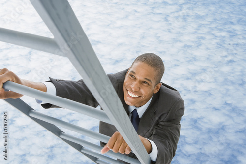 Photo: Mixed race businessman climbing ladder into the clouds Mixed race businessman climbing ladder into the clouds