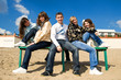 Group of five smiling young people sitting on a bench