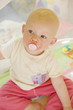 portrait of toddler with pacifier sitting in cot