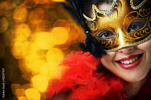 Foto: Beautiful young woman in carnival mask over gold background Beautiful young woman in carnival mask over gold background