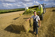 Photo: Farmer holding moisture reading equipment next to straw bale on baler in rural field Farmer holding moisture reading equipment next to straw bale on baler in rural field