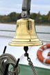 Goldene Schiffsglocke an Bord, im Hintergrund Rettungsring Goldene Schiffsglocke an Bord, im Hintergrund Rettungsring