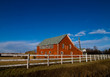 View of a barn with fence on sunny day with blue sky.