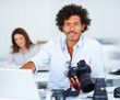 Handsome magazine editor holding a camera, colleagues in the bac