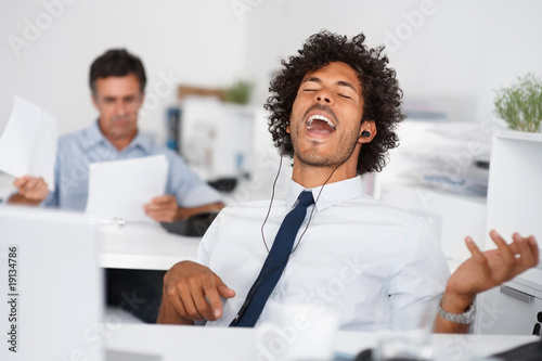 Photo: Male executive wearing headphones and listening to music at offi Male executive wearing headphones and listening to music at offi