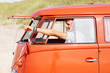 Smart happy guy driving a mini van at the beach, pointing outsid