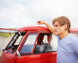 Handsome young man beside his red mini van at the beach