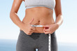 Mid section of a female measuring belly with a tape