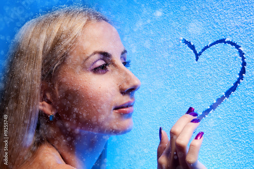 Photo: Beautiful blond woman draws heart on the frozen glass Beautiful blond woman draws heart on the frozen glass