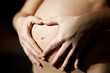 Hände formen ein Herz auf Babybauch