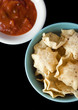 A bowl of tortilla chips with salsa bowl on black background