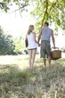 A young couple holding hands, carrying a picnic basket