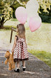 Child dragging a teddy and carrying a bunch of balloons.