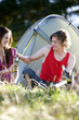 A young couple sitting in front of a tent, drinking beer