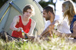 Three young people sitting in front of a tent, drinking beer