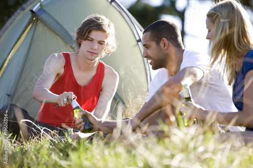 Photo: Three young people sitting in front of a tent, drinking beer Three young people sitting in front of a tent, drinking beer