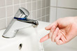 Frauenhand prüft Wassertemperatur am Wasserhahn