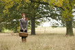 A young woman standing in a field, holding a wicker basket