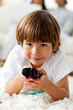 Foto: Smiling little boy holding a remote lying on the floor Smiling little boy holding a remote lying on the floor