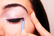 Young woman applying makeup on eye with a cosmetic black pencil