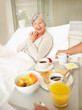 Senior relaxed female in bed being served breakfast