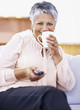 Elderly woman holding TV remote while drinking coffee