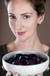 A mid adult woman holding a bowl of plums