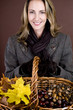 A woman holding a basket of conkers, acorns and autumn leaves